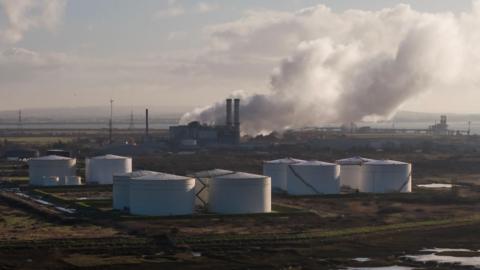 Aerial view of large white storage tanks at Grain LNG importation terminal with clouds of steam rising in the air in the background