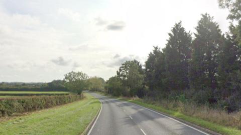 A rural road with trees and grass lining each side.