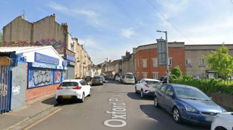 A Google Maps screengrab of Oxford Place in Easton, Bristol, a narrow residential street lined with parked cars with a garage on the corner. 