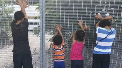 Children detained in Nauru hold their hands up against a fence