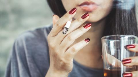 A woman smoking with a pint of beer in her hand