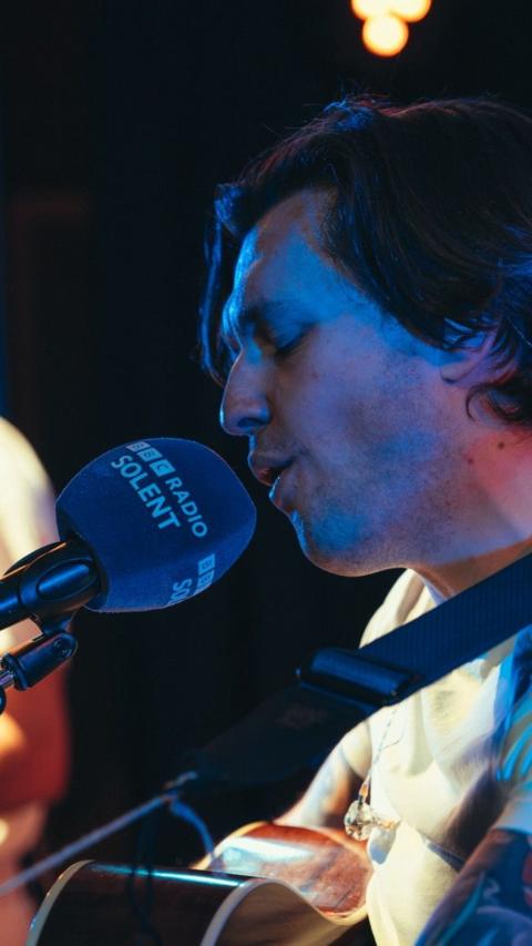 Close up of singer Billy Gregory singing in front of a BBC Radio Solent purple microphone.