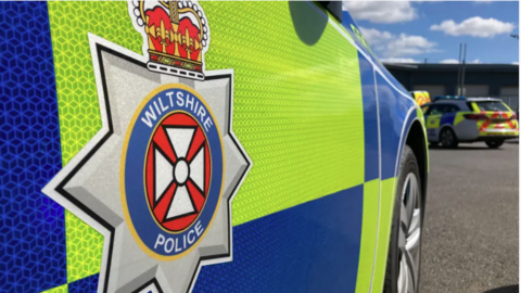 The side of a police car. It shows the Wiltshire Police emblem.