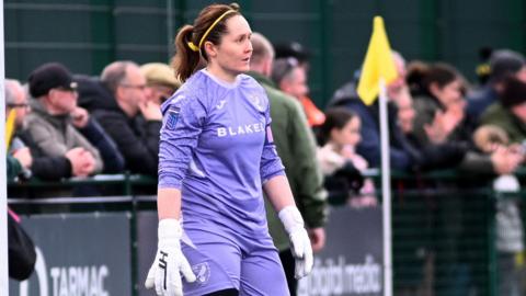 Sarah Quantrill, wearing a purple Norwich City Women's goalkeeper's kit, stands in her penalty area during a match