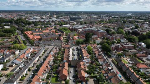 A drone view shows rows of terraced housing in Norwich city centre, with the wider skyline in view, which shows landmark buildings like the City Hall, Norman castle and cathedral spire in the distance.