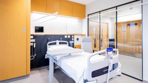 A medical room is pictured with shelving and a bed