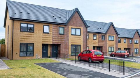 A row of new houses with grass gardens and cars parked on the drives