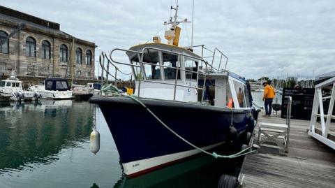 Saltash ferry at Royal William Yard in Plymouth. A black vessel docked on wooden walkway