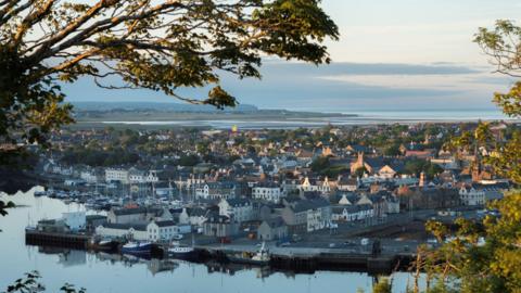 A view across Stornoway harbour and the town's houses and other buildings. The image has been taken through trees.