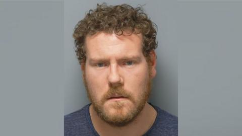 Mugshot of Louis Cann - he is white with brown curly hair and brown stubble.