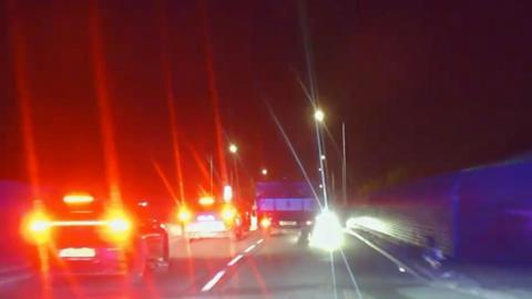Cars with break lights on, driving on a road at night time whilst a truck is driving on the wrong side of the road