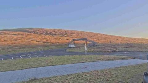 The Mountain road, at sunset, you can see a grassy bank in the background and the road, with a black bridge to cross it.