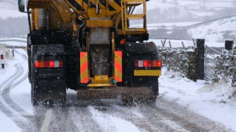 A generic image of a gritter spreading salt on a road. There are fields covered in snow in the distance.