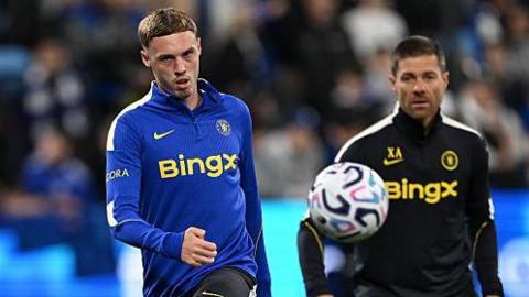 Cole Palmer being watched by Xabi Alonso during the warm-up before a Chelsea match