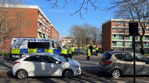 A marked police van and several police officers in the road outside a block of flats