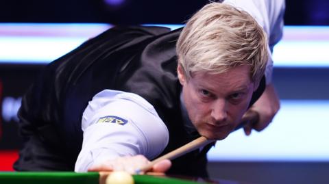 Neil Robertson looks down his snooker cue as he takes aim at the white ball. He has blond hair and is wearing a white shirt under a black waistcoat.