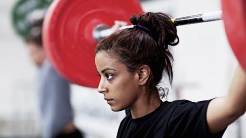 A woman in a black top lifting a barbell.