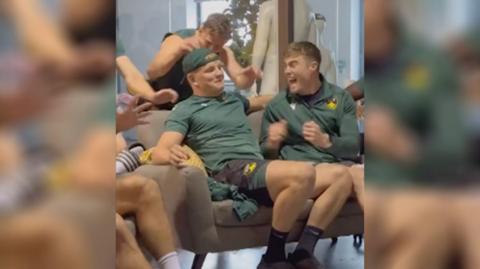 Northampton rugby players sat a sofa cheering