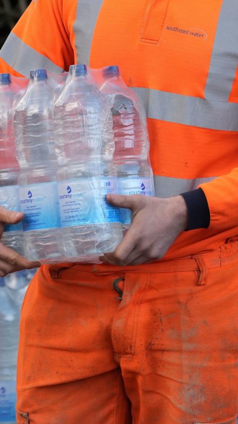 A worker carrying a six pack of water.