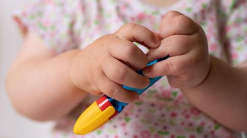 A baby plays with a pen-shaped toy. Only their hands and part of their chest are visible.
