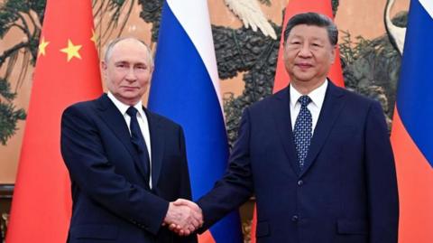 Vladimir Putin and Xi Jinping shake hands, with the flags of Russia and China in the background