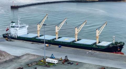 A container ship with four large cranes berthed at a dock