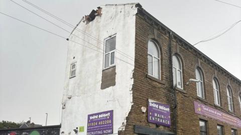 A photo of a building with a hole at the top of the structure where the chimney had been in place.