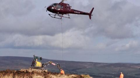 A helicopter lowering stones onto the ground at Ilkley Moor