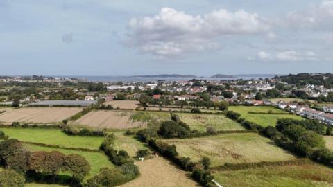 Drone shot overlooking part of Guernsey with fields in the foreground. The islands of Herm, Jethou and Sark are in the background.