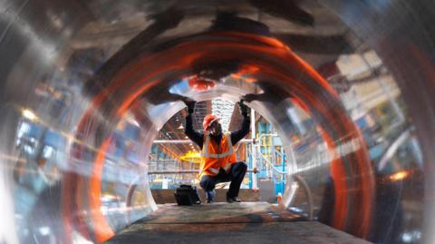 An engineer in a hard hat and high-vis jacket testing forged steel at a factory in Sheffield