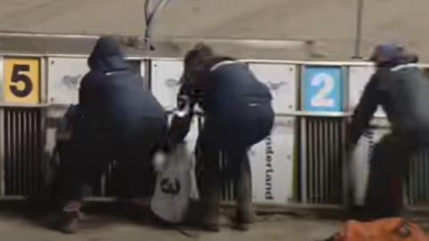 Three people leaning over the racing traps as they try to help the dogs.
