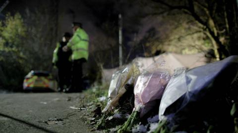 Bouquets of flowers left on Ravenscraig Road, near Ashtons Field in Salford, Greater Manchester, where the remains of a baby were found in a field. Police officers and a police car are in the background of the photograph.
