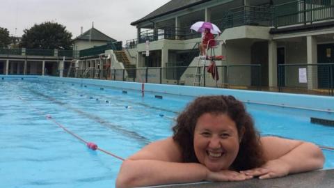 Keely, a woman, posing at the edge of the swimming pool. You can see the pool behind her and a life guard sitting on a high chair by the side of the pool.