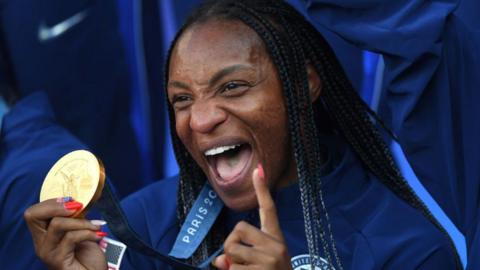 Crystal Dunn smiles while holding an Olympic gold medal