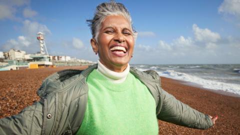 A mature woman smiles as she faces the wind on a beach