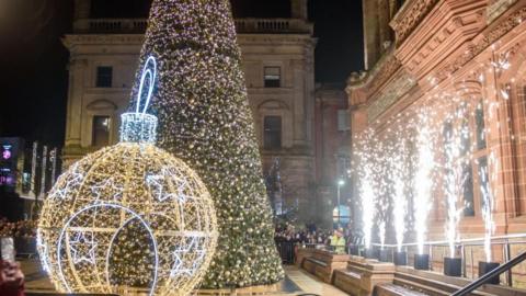 The Christmas decorations outside Derry's Guildhall are fully illuminated. There is a crowd standing around watching