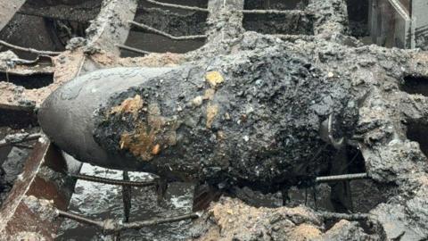Bomb on top of a metal crate on a boat. Rubble around him.