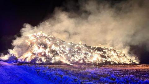 Haystack on fire with field and ash on the ground - which looks blue in colour 