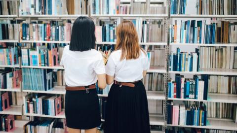 Two female students searching for books in a library - stock photo