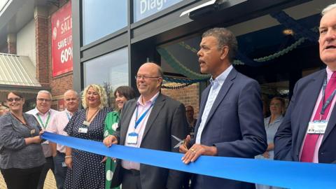 Chris Kamara prepares to cut a blue ribbon with a pair of scissors. 