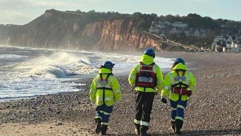 Three people in hi vis on Budleigh Salterton beach.
