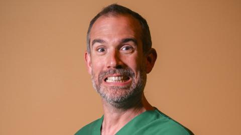 Dr Xand pulling a grimace in green medical scrubs.