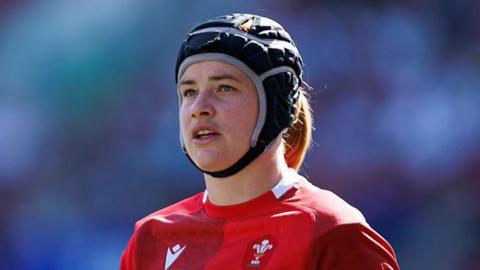 Bethan Lewis, wearing a scrum cap, standing on the pitch wearing a Wales shirt during a Six Nations match