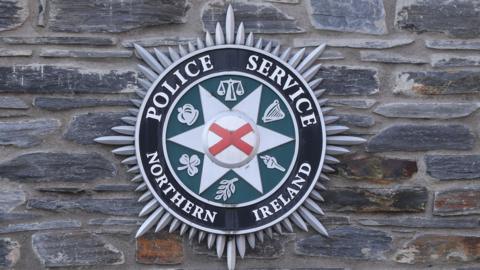 Police service of Northern Ireland badge on brick wall.