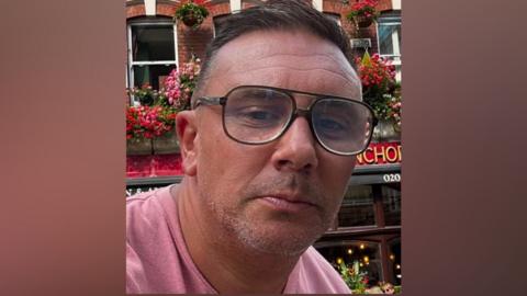 Head and shoulders shot of Graeme Hull. He is wearing glasses and had short dark hair. He is wearing a pink t-shirt.