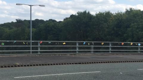 A series of small, colourful notes attached to a bridge over the A14 in Northamptonshire.