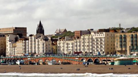 A picture of Brighton beach and pier; walkways down to the pier are visible, as is the sand. A number of apartment buildings are also visible below the skyline.