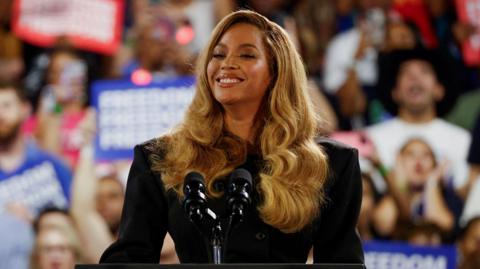 Beyonce smiles on the stage of a Harris rally