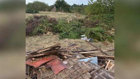 Broken wood and waste has been left in a pile on field 
