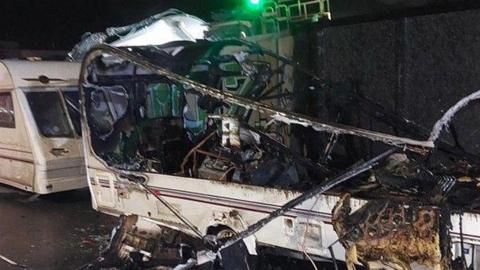 A burned out caravan, with only its frame and base remaining. Another caravan is parked behind and is intact.